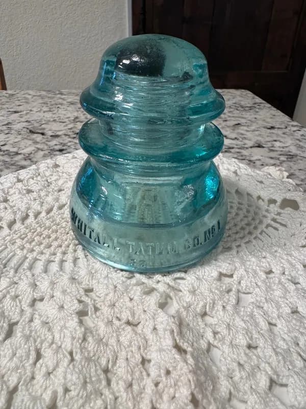 A vintage aqua Whitall Tatum glass insulator on a lace doily