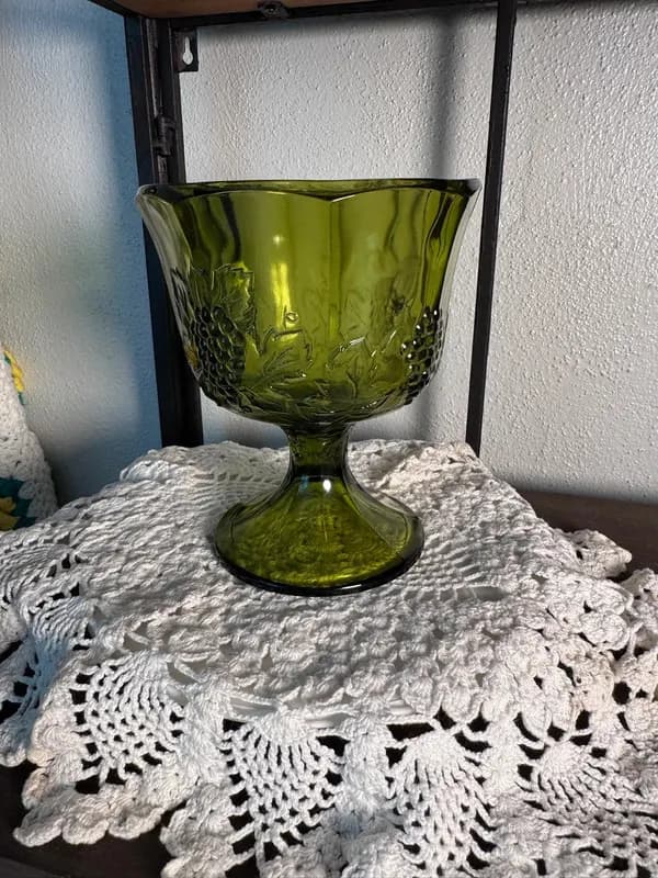 An olive green Indiana Glass grape pedestal compote bowl on a lace doily