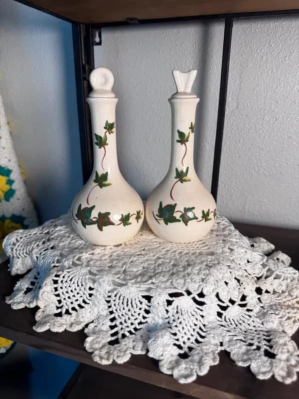 A pair of cream crackle-glaze ceramic oil and vinegar cruets with ivy stoppers on a lace doily
